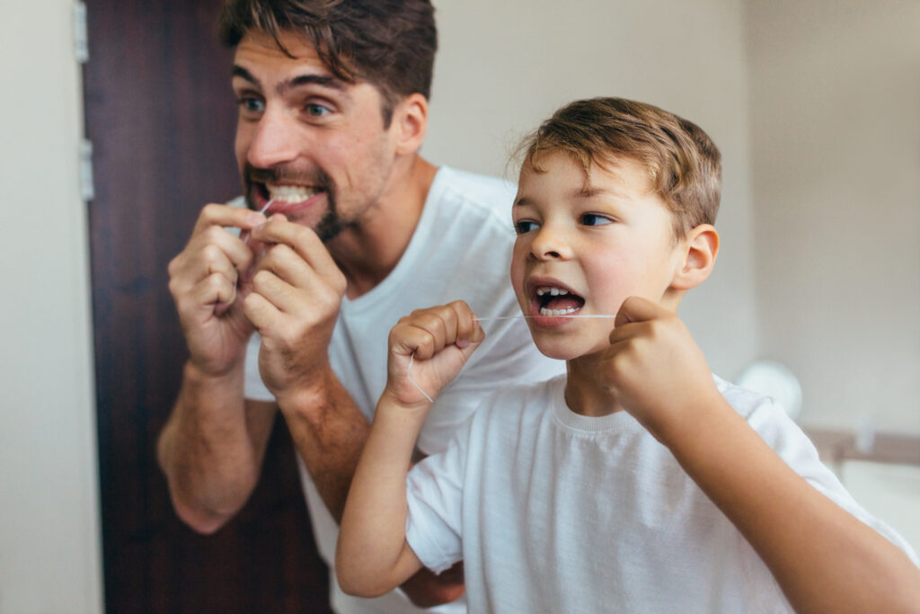 Vater und Sohn putzen sich vor dem Spiegel die Zähne.